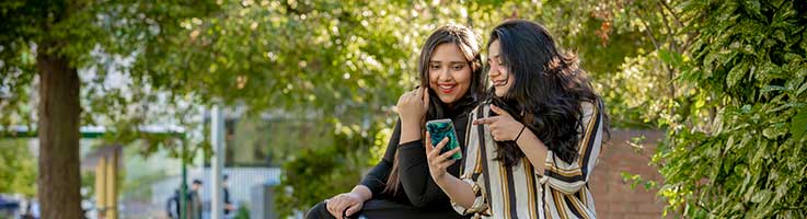 Two students sat outside of the hub looking at a phone