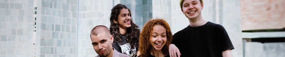 Four students smiling outside on campus.