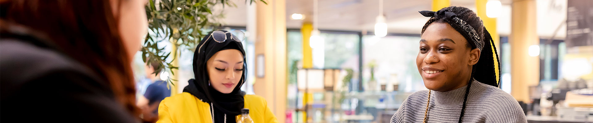 Three students sat around a table in a cafe in The Hub on campus.