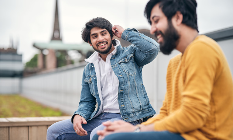 Two students sitting in the rooftop garden at The Hub, with the spire of the Coventry Cathedral ruins in the background.