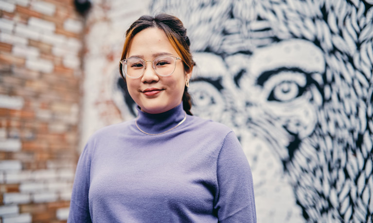 Smiling Asian student standing in front of a mural