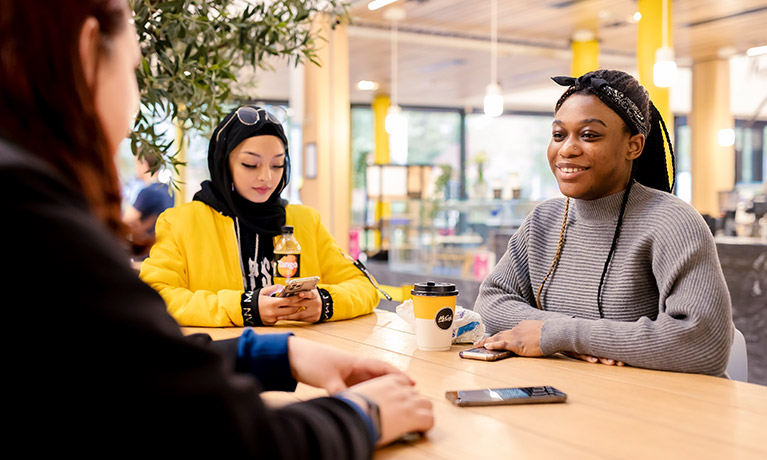 Three students sat around a table in the cafe on campus at The Hub.