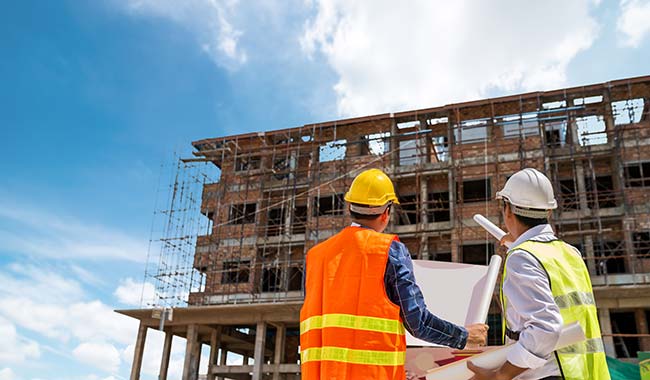 Two construction workers looking at a project plan looking a building under construction