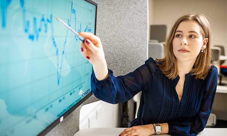 Female student using pen to point at screen with financial data on.