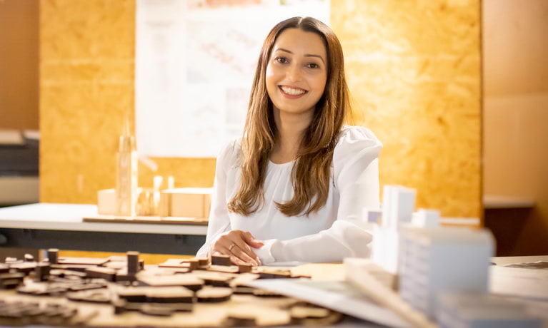 Female student sitting in front a architectural design table smiling at the camera 