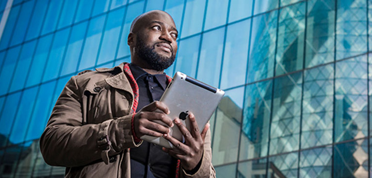 Man standing infront of a building working on an ipad