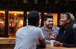 Three people standing at a tall table having coffee