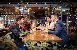 Four young people talking to each other over drinks in a busy bar