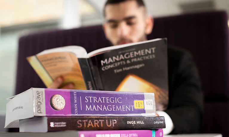 man reading  a book infront of a stack of books