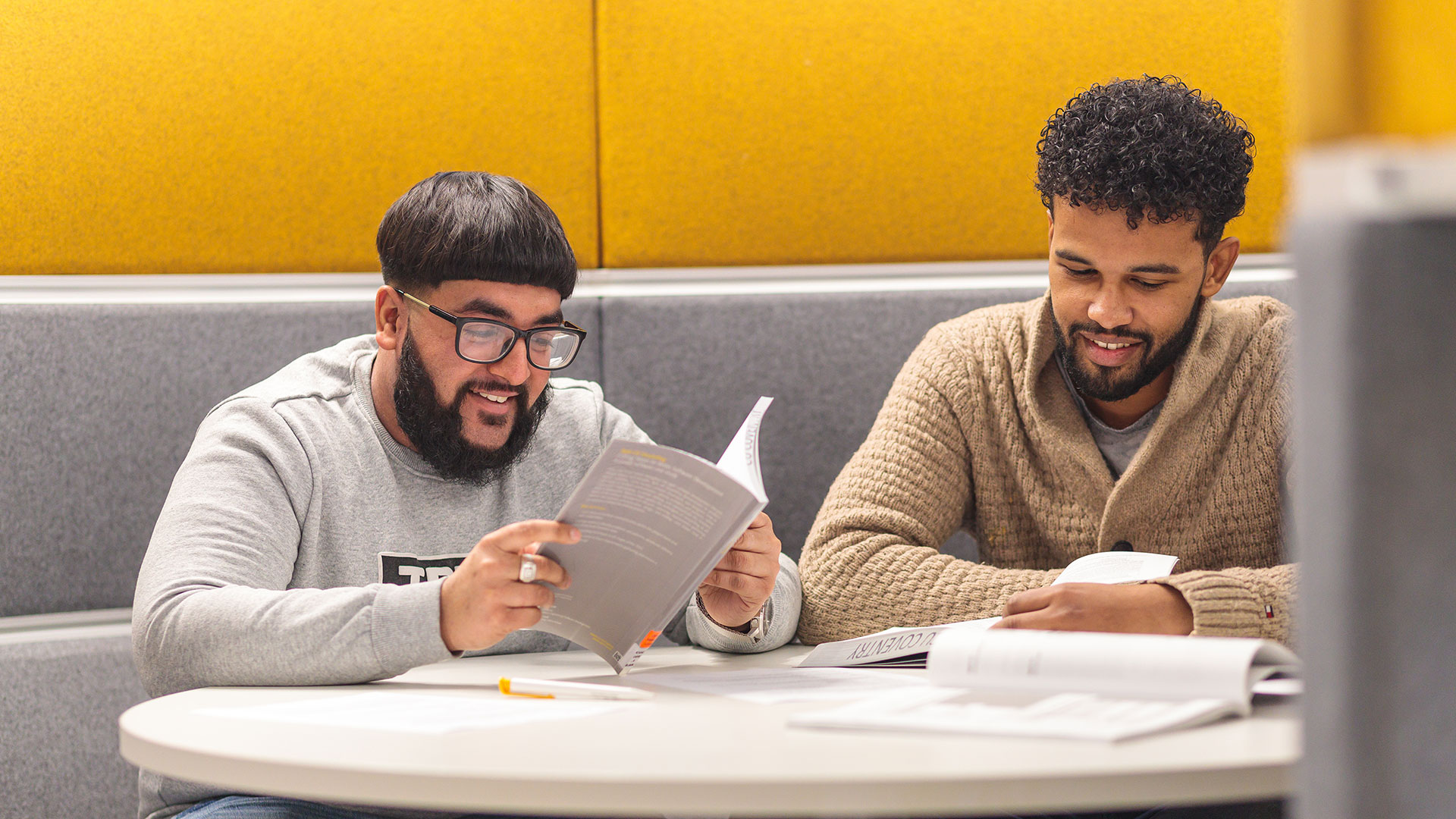 Two smiling students looking at materials while sitting at a booth together