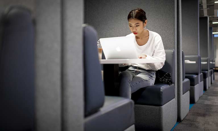 Female student sitting in a booth on a laptop