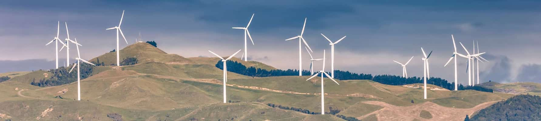 Hilly landscape covered with wind farm turbines with a dark cloudy sky in background