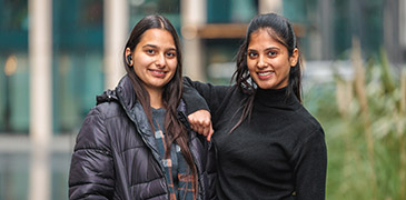 One female student leaning resting her arm on the shoulder of another female student