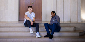 Two male students at a flight of stairs indoors talking