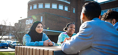 Group of students sat oustisde on a bench talking