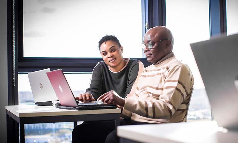 Two students sat together looking at their laptops