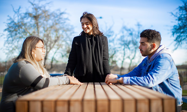 group of students sat on a bench outside talking