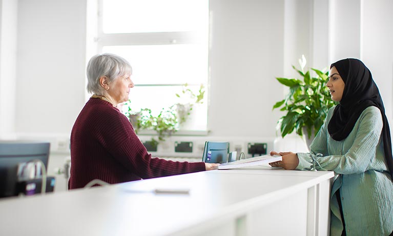 Student stood talking to a member of staff at a reception desk