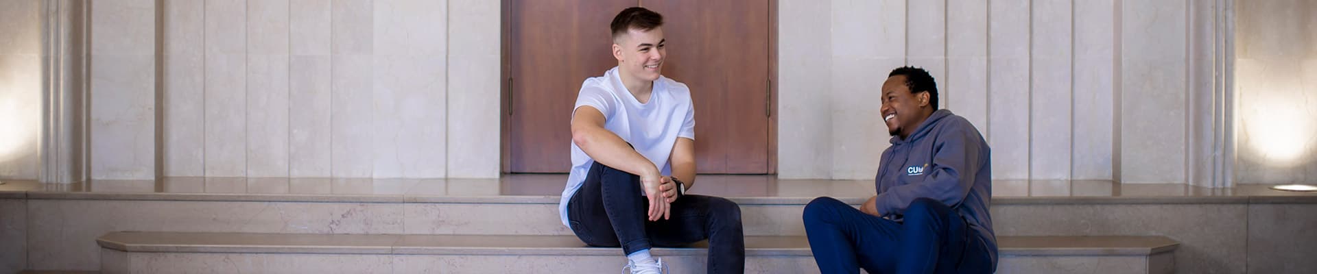 Two students sat on a few steps inside of a building