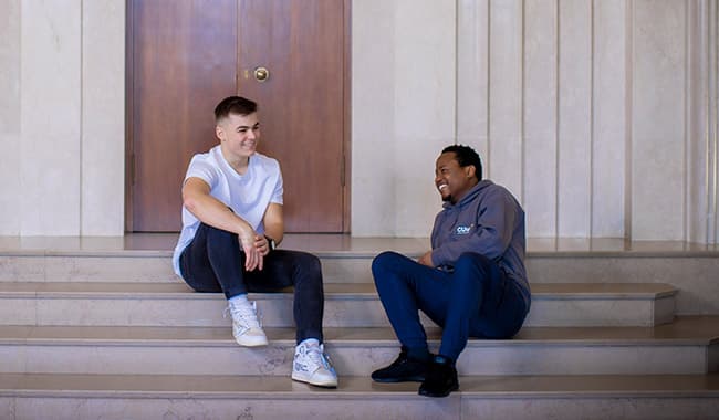 Two students sitting down on a step inside a building