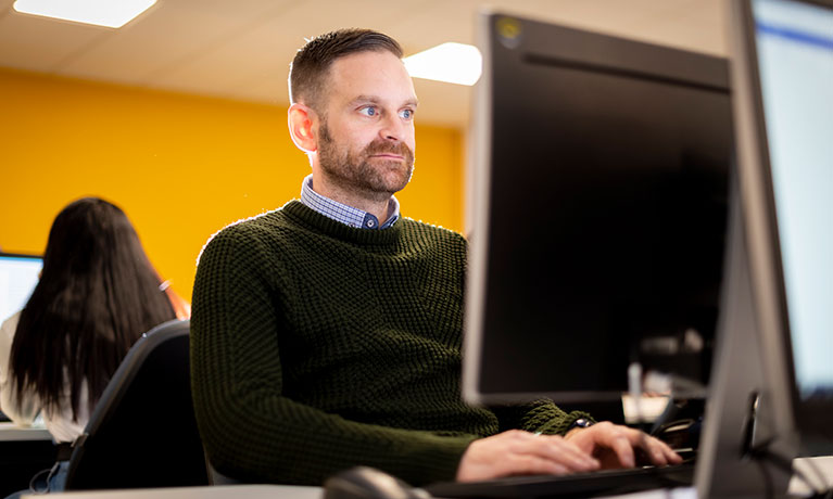 Male student sat working on a computer screen