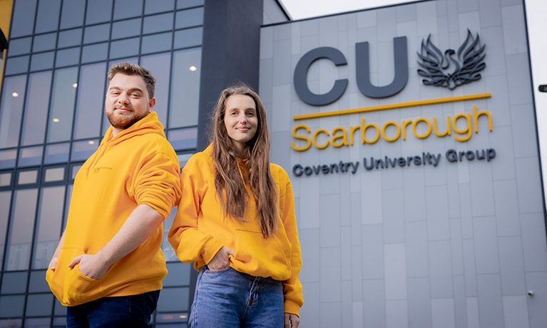 Two students wearing yellow hoodies standing outside of the CU Scarborough building