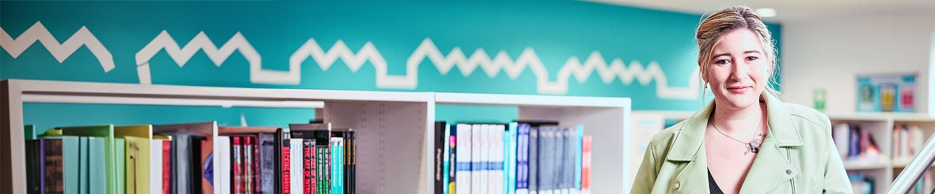 Female student leaning against a bannister with a book shelf behind