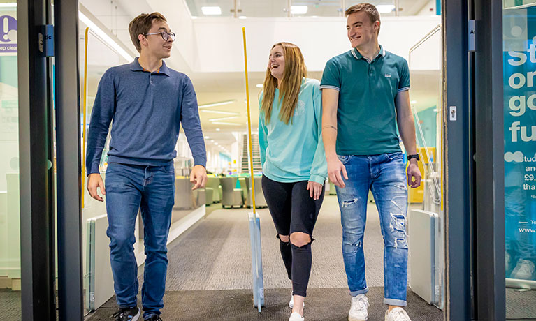 Three students walking out of a building whilst talking