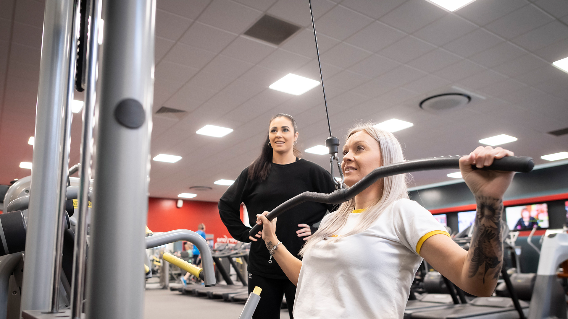 Sports coach watching a female working  at a chest and shoulder machine