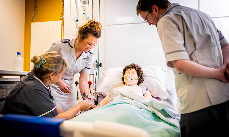 Students in the mock nursing ward working on a manikin in a hospital bed.