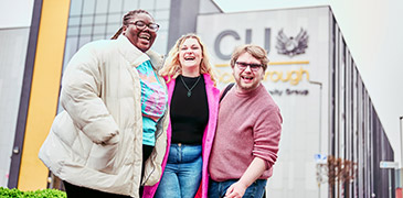 Three students stood outside the CU Scarborough on a cloudy day smiling