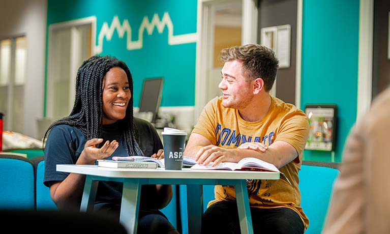 Two students sat at a table chatting with open books