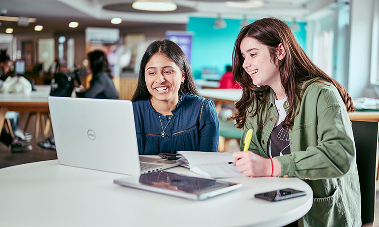 Two female students sat at desk smiling