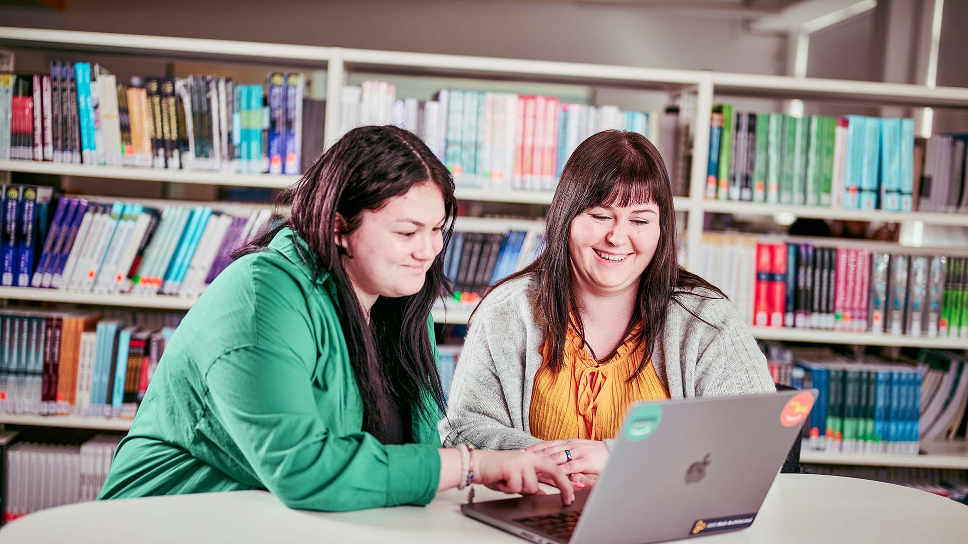 Two students sat at a desk working on a laptop