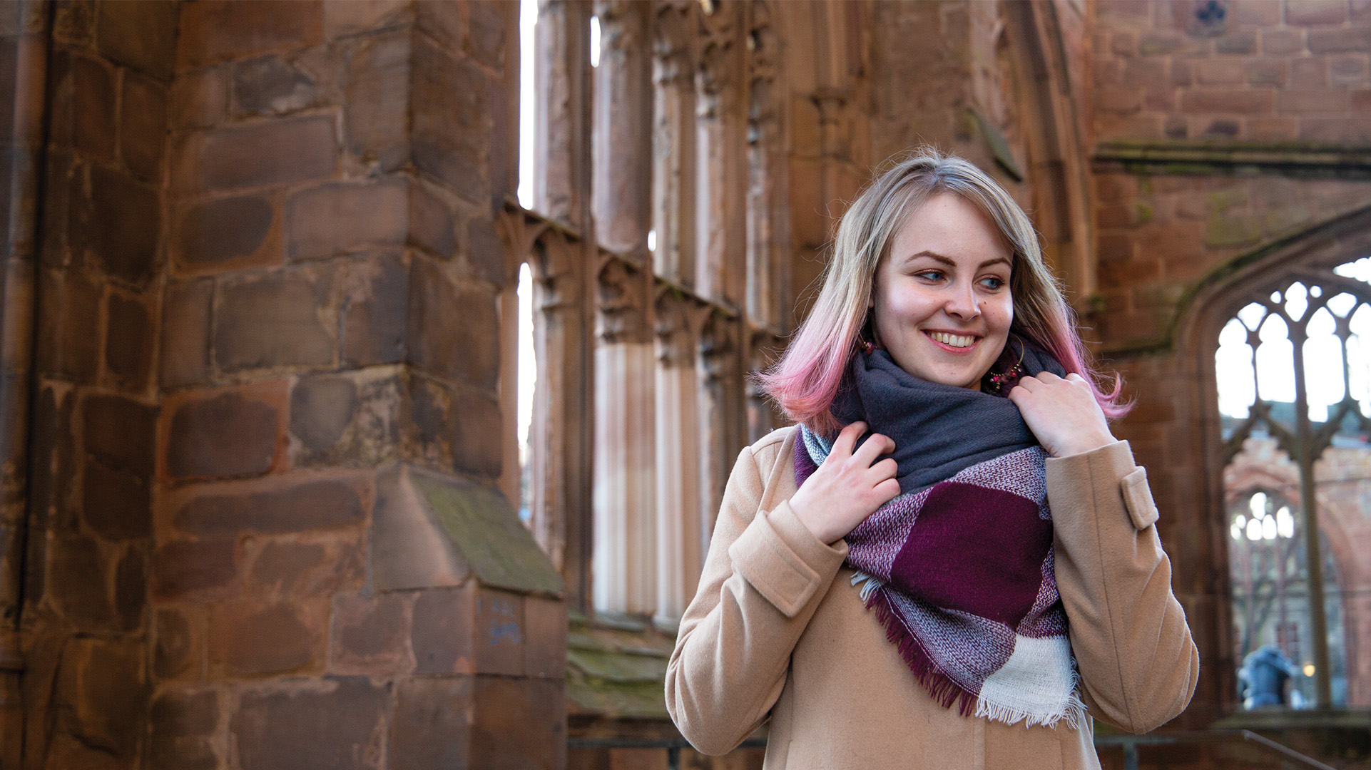 A student wearing a scarf and smiling in the Coventry Cathedral ruins.