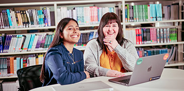 Two students sat at a table working on their laptops