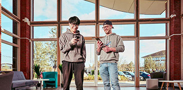 Two male students stood in an open area looking down at their phones