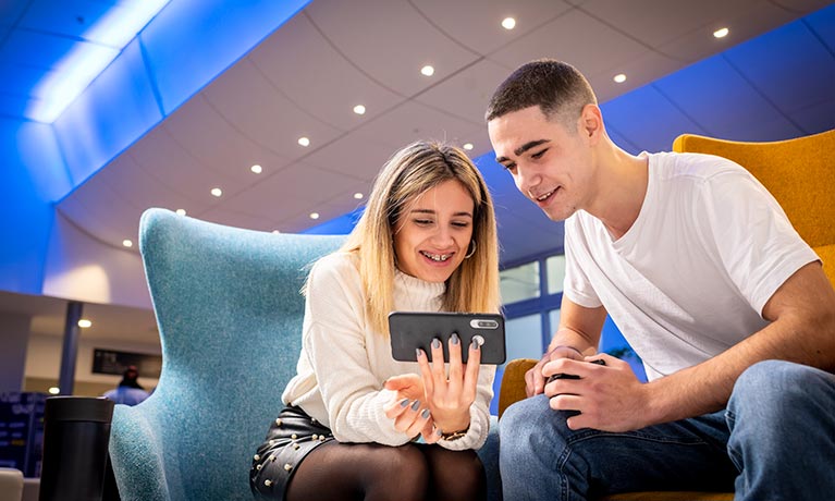 Two students sat together looking at a phone