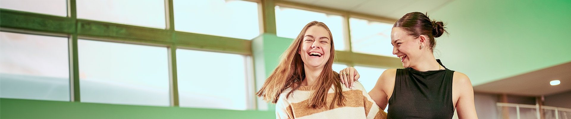 Two students walking through reception talking and laughing