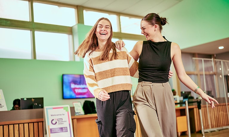 Two students walking through a reception area talking and smiling