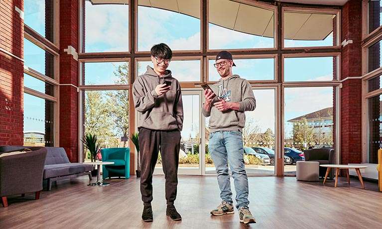 Two students stood in an open space using their phones