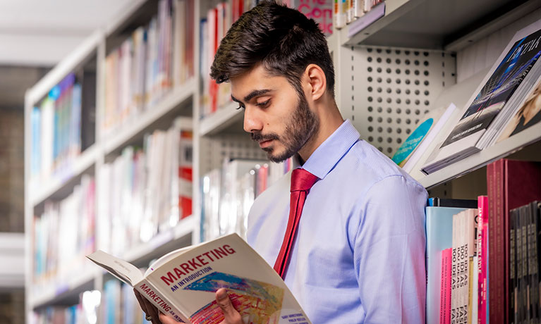 Student reading a book in a library aisle