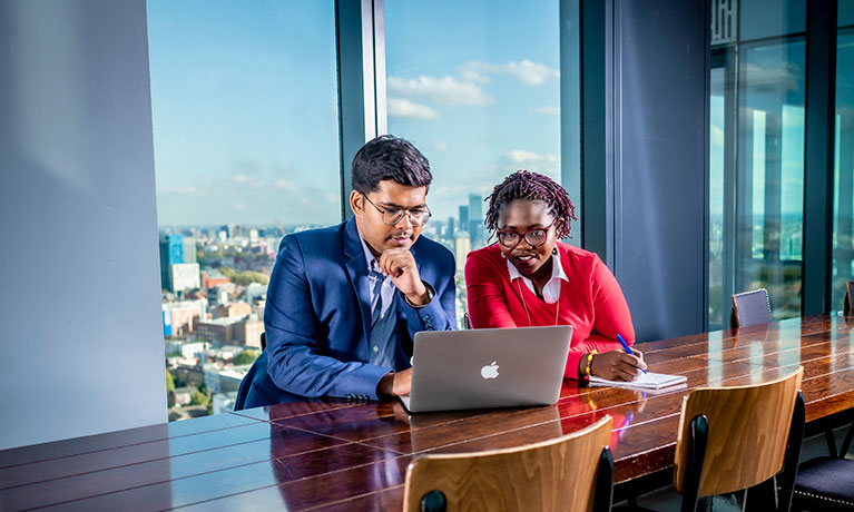 smartly dressed man and woman looking at a laptop in an office