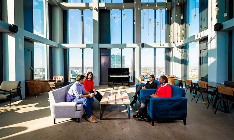 Group of students sat on two sofas talking