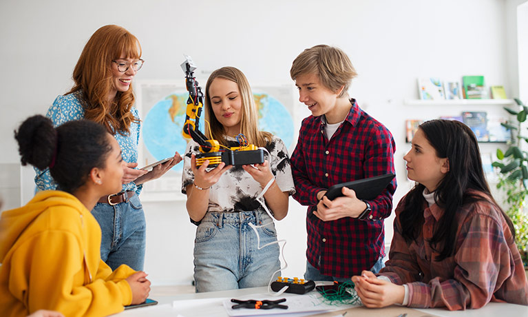 A trainee teacher using a tablet to control a robotic model their class is making