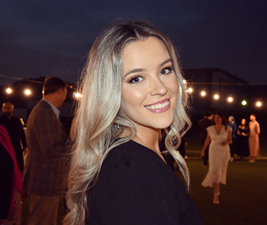 A profile photo of Aava Hearns smiling at an outdoor festival with strings of lights in the background.