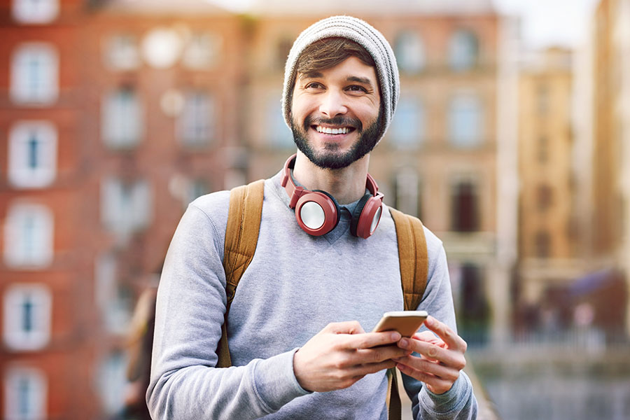 A younger man with a beard, wearing a beanie hat and headphones, using his mobile phone.