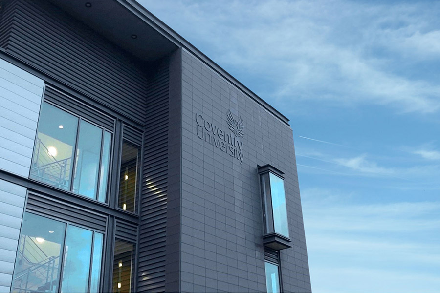 The corner of the NITE headquarters with the Coventry University logo, against a blue cloudy sky. 