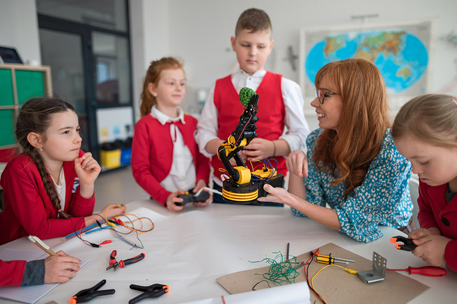 A teacher sat with students in red school uniforms, as they work on robotic models.