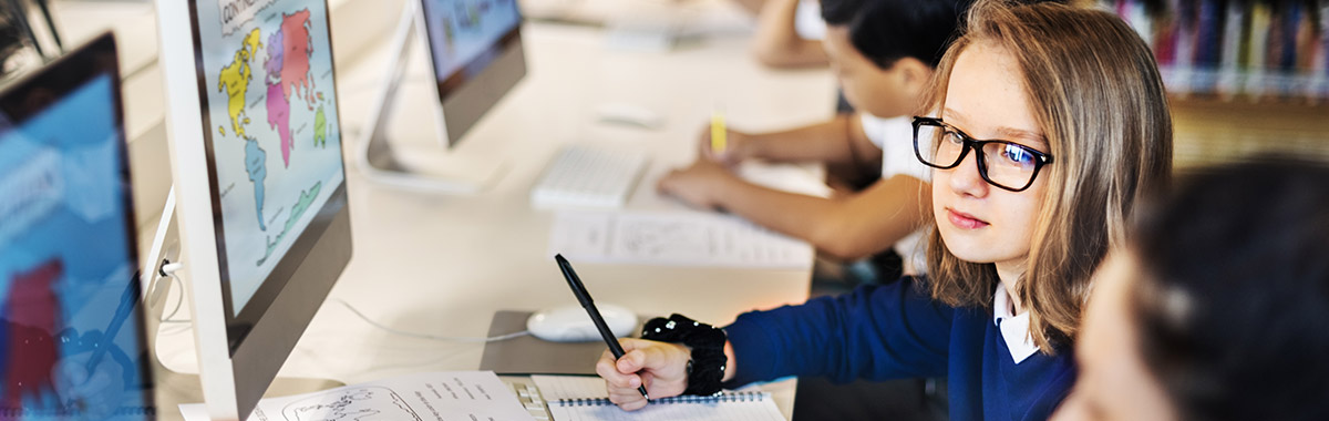 Young students sat in a row using macs in a lesson.